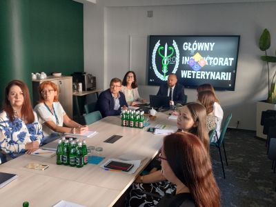 Zdjęcie przedstawiających uczestników spotkania siedzących przy stole konferencyjnym w sali.