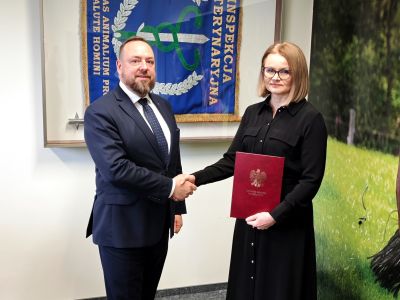 Zdjęcie przedstawia Głównego Lekarza Weterynarii ściskającego dłoń nowo powołanej Wojewódzkiej Lekarz Weterynarii na tle gabloty z flagą Inspekcji Weterynaryjnej Zdjęcie przedstawia Głównego Lekarza Weterynarii ściskającego dłoń nowo powołanej Wojewódzkiej Lekarz Weterynarii na tle gabloty z flagą Inspekcji Weterynaryjnej